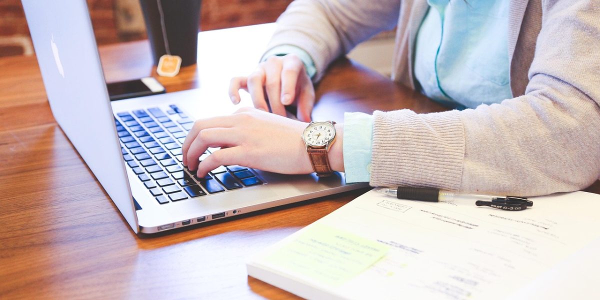 A person at a desk with multiple open documents and a laptop, actively cross-referencing information to verify facts.