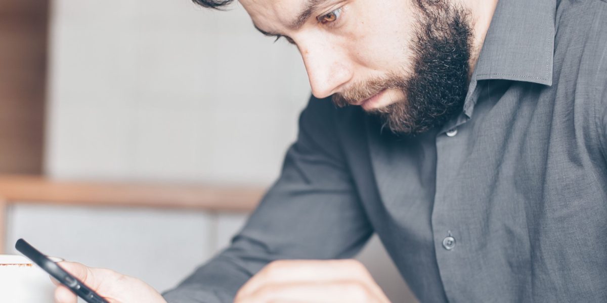 A person looking at their phone with a thoughtful and skeptical expression, reflecting media distrust.